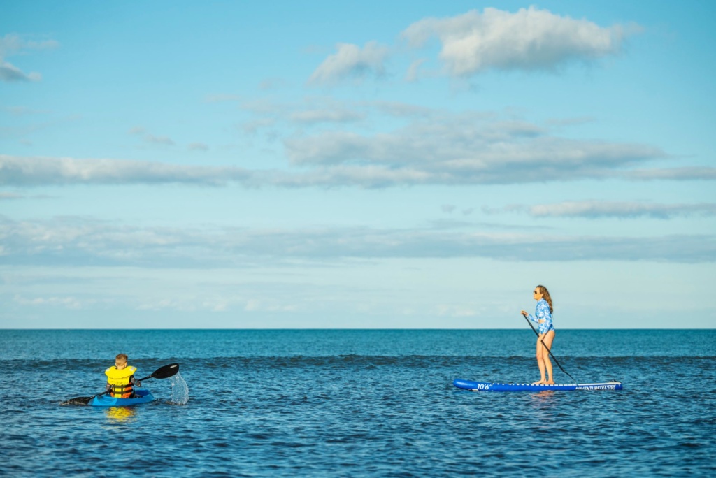 A person kayaking and a woman stand-up paddleboarding